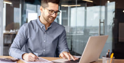 Contabilidade Online homem branco usando óculos e camisa azul mexendo no notebook